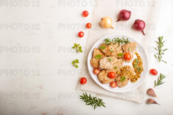 Fried pork chops with tomatoes and herbs on a white ceramic plate on a white wooden background and linen textile. top view, flat lay, copy space