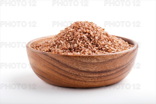 Wooden bowl with unpolished brown rice isolated on white background. Side view, close up