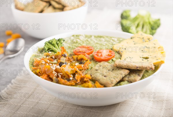 Green broccoli cream soup with crackers and cheese in white bowl on a gray concrete background and linen napkin. side view, close up, selective focus