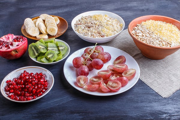 A set of plates with muesli, grapes, kiwi, pomegranate, banana on a black wooden background. close up