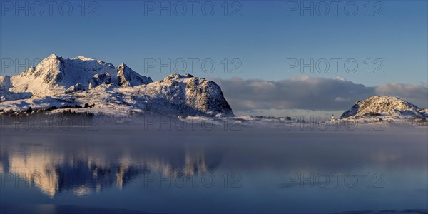 Leichter nebel in der verschneiten Berglandschaft auf den vesteralen mit schoener Spiegelung im Fjord
