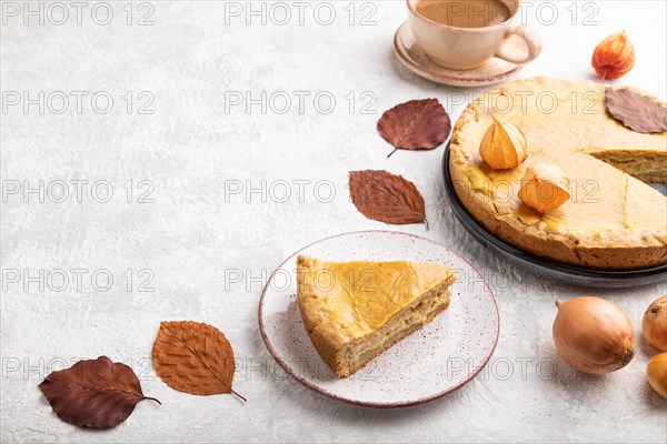 Autumn onion pie decorated with leaves and cup of coffee on gray concrete background. Side view, copy space, close up