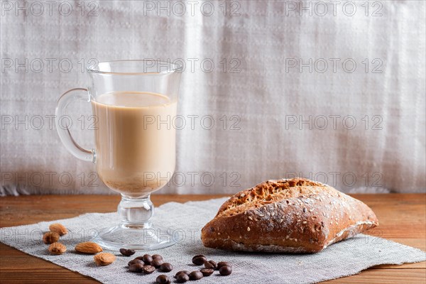 Glass cup of coffee with cream and bun on a wooden background and linen textile. close up, copy space