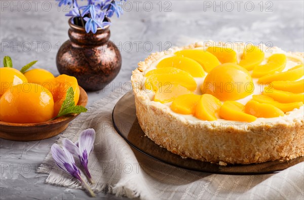 Round peach cheesecake and ceramic vase with blue flowers on a gray concrete background. side view, close up. linen napkin