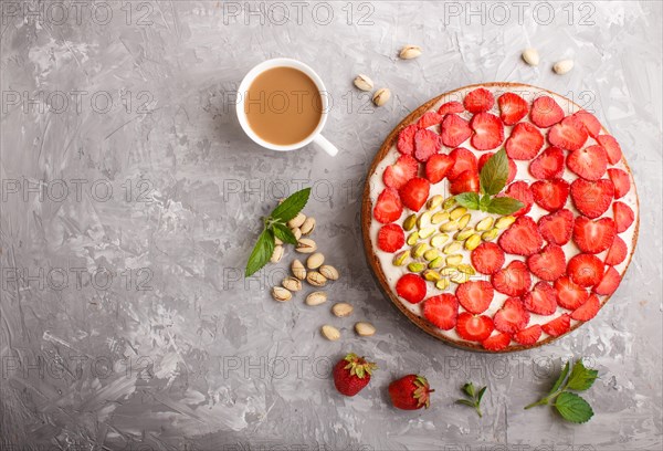 Homemade cake with yoghurt cream, strawberry, pistachio and a cup of coffee on a gray concrete background. top view. flat lay, copy space