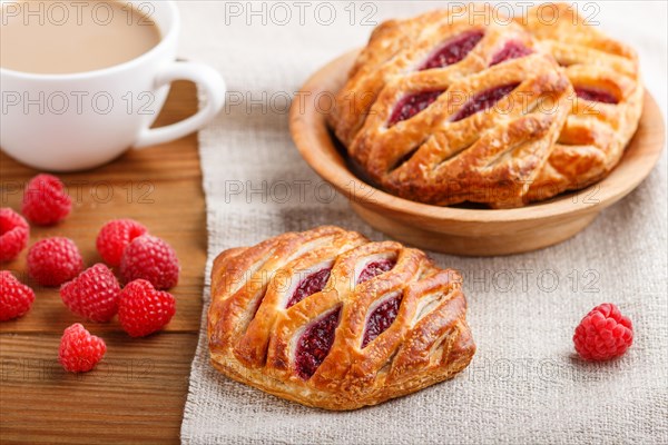 Puff pastry buns with strawberry jam on wooden background with linen textile and a cup of coffee. side view, close up, selective focus