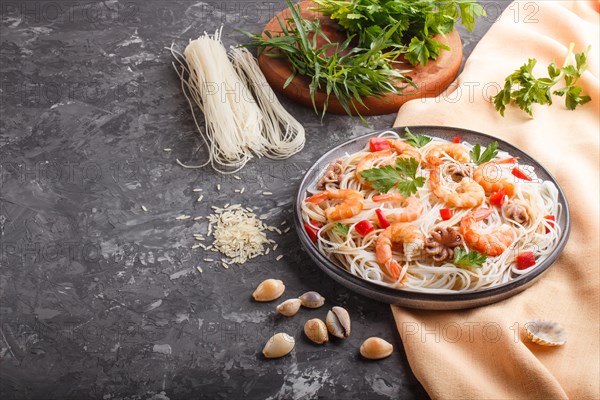 Rice noodles with shrimps or prawns and small octopuses on gray ceramic plate on a black concrete background and orange textile. side view, copy space