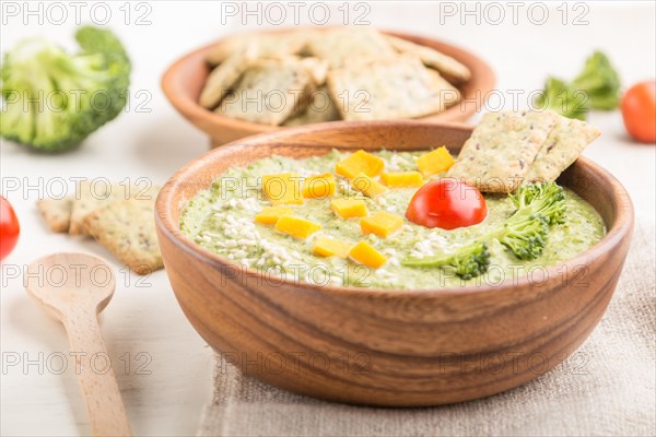 Green broccoli cream soup with crackers and cheese in wooden bowl on a white wooden background and linen napkin. side view, close up, selective focus
