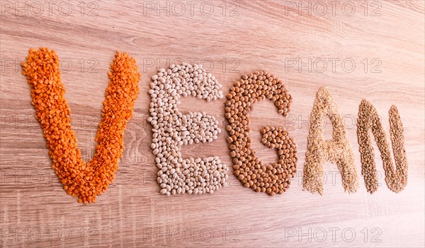 Word Vegan made of lentils, buckwheat, beans, rice and chickpeas on a wooden background