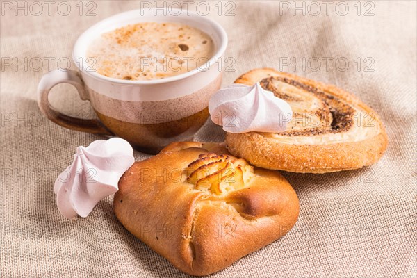 Sweet buns, meringues and coffee cup on a wooden board and linen tablecloth