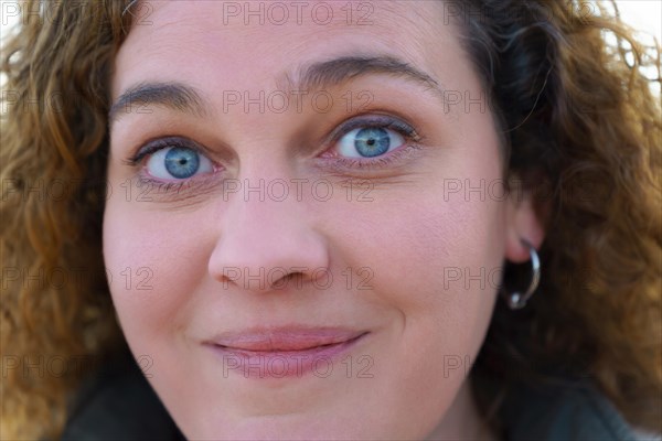 Close-up portrait of an attractive woman with blue eyes and curly blonde hair smiling at the camera