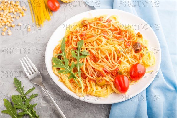 Corn noodles with tomato sauce and arugula on a gray concrete background and blue textile. Side view, close up, selective focus