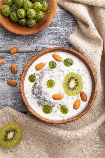 Yogurt with kiwi, gooseberry, chia and almonds in wooden bowl on gray wooden background and linen textile. top view, flat lay, close up