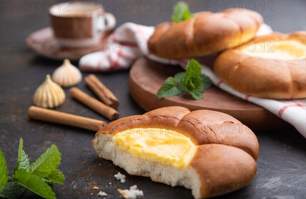 Sour cream bun with cup of coffee on a black concrete background and linen textile. Side view, close up, selective focus