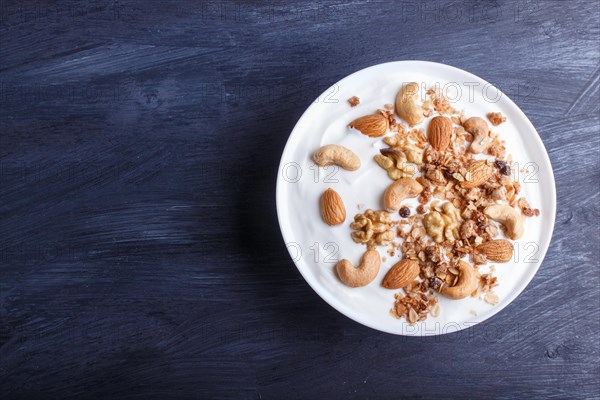 White plate with greek yogurt, granola, almond, cashew, walnuts on black wooden background. top view. copy space