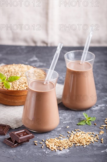 Organic non dairy oats chocolate milk in glass and wooden plate with oats seeds on a black concrete background. Vegan healthy food concept, close up, side view