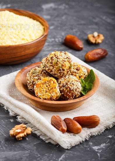 Energy ball cakes with dried apricots, sesame, cornflakes, linen, walnuts and dates with green mint leaves in a wooden bowl on a black concrete background. linen napkin, side view, close up, selective focus, vegan homemade candy