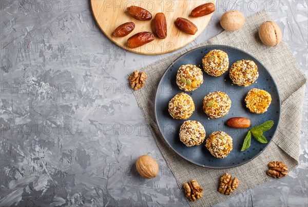 Energy ball cakes with dried apricots, sesame, linen, walnuts and dates with green mint leaves on a blue ceramic plate on a gray concrete background. linen napkin, top view, copy space, flat lay. vegan homemade candy