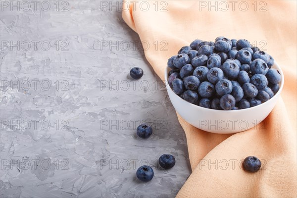 Fresh blueberry in white bowl and orange pastel textile on gray concrete background. side view, copy space