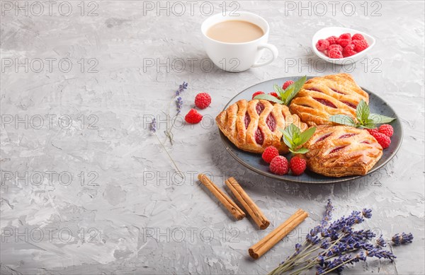Puff pastry buns with strawberry jam on blue ceramic plate on gray concrete background, cup of coffee, lavender, cinnamon, mint leaves. side view, copy space