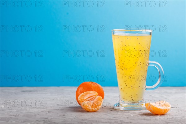 Glass of tangerine orange colored drink with basil seeds on a gray and blue background. Morninig, spring, healthy drink concept. Side view, copy space