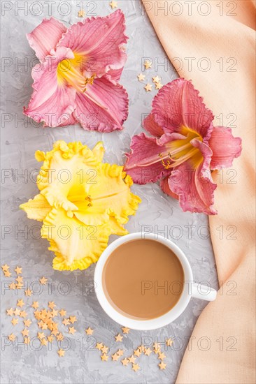Yellow anf purple day-lilies cup of coffee on a gray concrete background, with orange textile. Morninig, spring, fashion composition. Flat lay, top view, close up