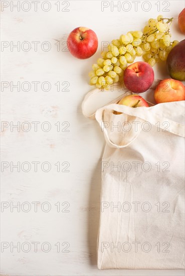 Fruits in reusable cotton textile white bag. Zero waste shopping, storage and recycling concept, eco friendly lifestyle. Top view, flat lay, copy space. Peach, apple, mango, grape