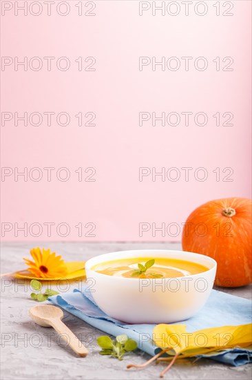 Traditional pumpkin cream soup with in white bowl on a gray and pink background with blue napkin. side view, close up, selective focus, copy space