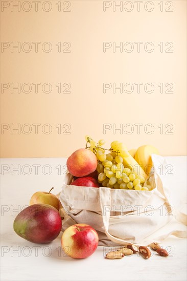 Fruits in reusable cotton textile white bag. Zero waste shopping, storage and recycling concept, eco friendly lifestyle. Side view, copy space. Peach, apple, mango, grape, banana