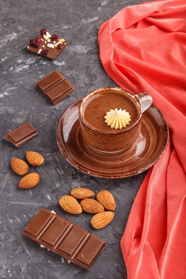 Cup of hot chocolate and pieces of milk chocolate with almonds on a black concrete background with red textile. side view, close up