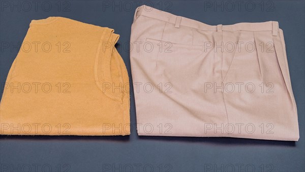 Brown sleeveless sweater next to pair of pleated beige pants on black background