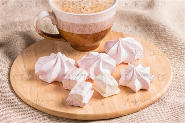 Sweet buns, meringues and coffee cup on a wooden board and linen tablecloth