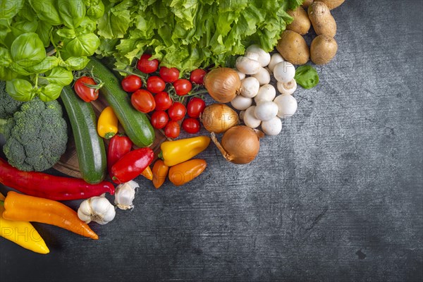 Fresh lettuce, courgettes, broccoli, tomatoes, peppers, mushrooms, onions and potatoes arranged on a wooden board symbolises health