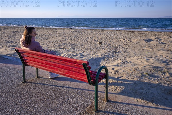 Young woman sitting on bench, bench, looking at the sea, coat, lonely, alone, beach, Peraia, also Perea, evening light, Thessaloniki, Macedonia, Greece, Europe