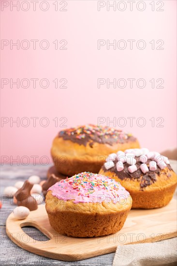 Homemade glazed and decorated easter pies with chocolate eggs and rabbits on a gray and pink background and linen textile. Side view, selective focus, copy space