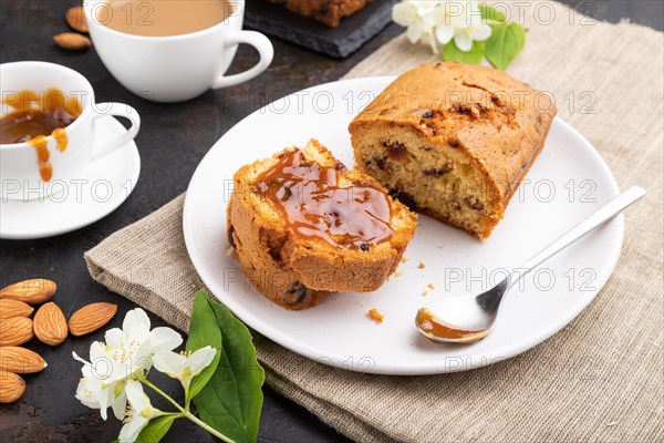 Homemade cake with raisins, almonds, soft caramel and a cup of coffee on a black concrete background and linen textile. Side view, close up