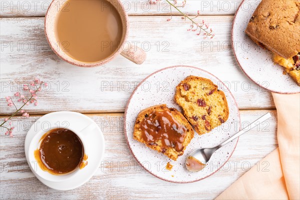 Homemade cake with raisins, almonds, soft caramel and a cup of coffee on a white wooden background and orange linen textile. top view, flat lay, close up