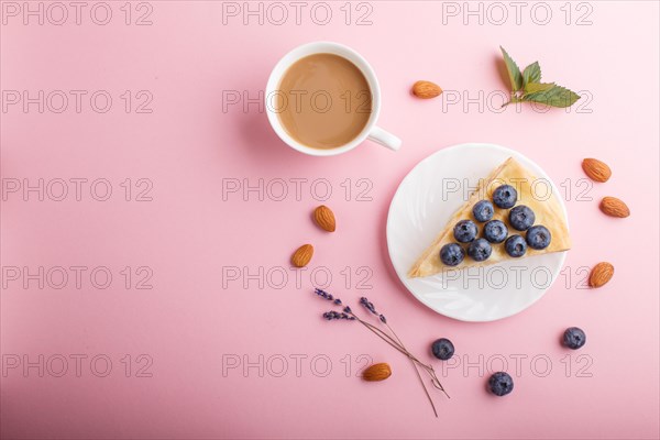 Homemade layered Napoleon cake with milk cream. Decorated with blueberry, almonds, walnuts, hazelnuts, mint on a pastel pink background and a cup of coffee. top view. flat lay, copy space