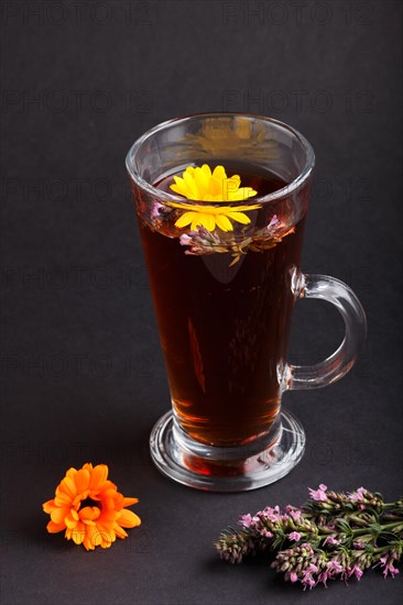 Glass of herbal tea with calendula and hyssop on a black background. Morninig, spring, healthy drink concept. Side view, selective focus, close up