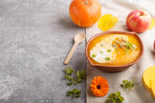 Traditional pumpkin cream soup with seeds in clay bowl on a gray concrete background with linen textile. side view, copy space