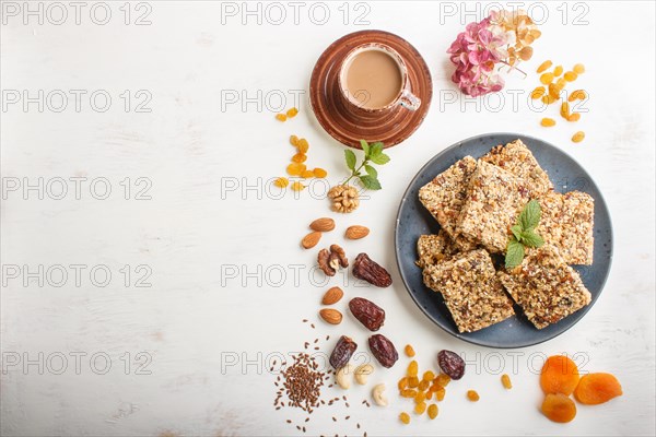 Homemade granola from oat flakes, dates, dried apricots, raisins, nuts in blue ceramic plate with a cup of coffee on a white wooden background. Top view, flat lay, copy space