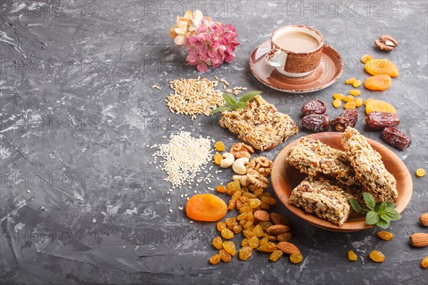 Homemade granola from oat flakes, dates, dried apricots, raisins, nuts with a cup of coffee on a black concrete background. Side view, copy space