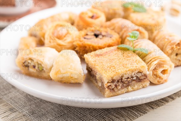 Traditional arabic sweets (kunafa, baklava) and a cup of coffee on a white wooden background and linen textile. side view, close up, selective focus