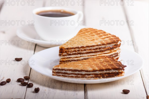 Waffle sandwiches with boiled condensed milk in plate on white wooden table with cup of coffee. closeup