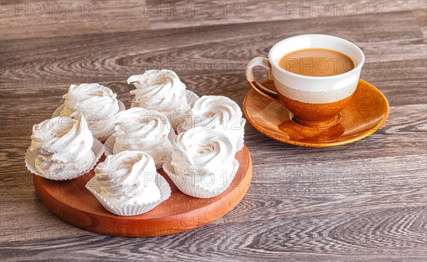 White marshmallows (zephyr) on a round wooden board with cup of coffee on a gray wooden background