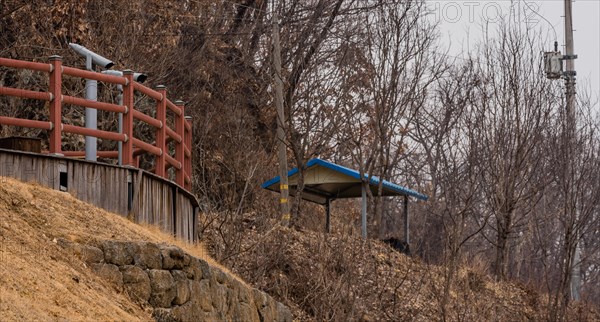 Wooden observation platform with two viewing binoculars behind red railing located in treed wilderness area in South Korea