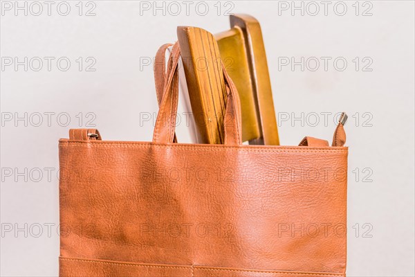 Brown leather shoulder bag hanging on back of chair with white background