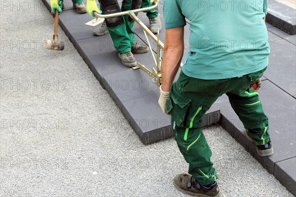 Workers lay heavy paving stones with a stone lifter