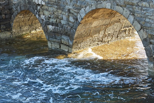 Sunlight shines through stone arches of an old bridge with foaming sea waves below, sea fortress Methoni, Peloponnese, Greece, Europe