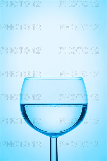 Wine glass half filled with water and a blue background
